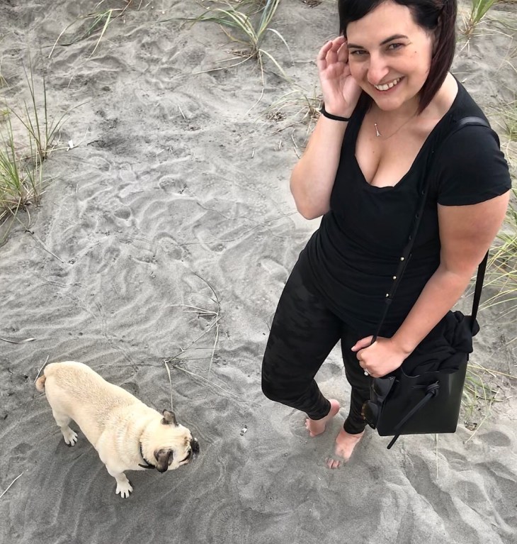 Girl on sand, smiling with pug dog